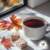 Cup of red tea on a white surface next to 2 off-brown fat bombs and 2 maple leaves (one bigger and the other one smaller) with a window in the background