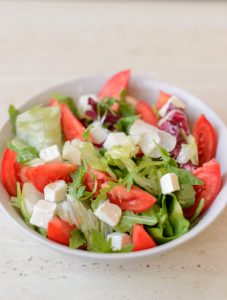 White porcelain bowl with finely cut tomatoes, lettuce, onions and cheese cubes consisting a fresh salad