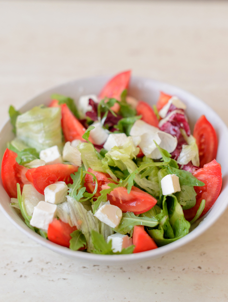 White porcelain bowl with finely cut tomatoes, lettuce, onions and cheese cubes consisting a fresh salad