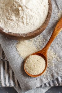 Wooden bowl and wooden spoon with white flour on a kitchen towel