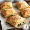 Five mini spinach parcels sprinkled with sesame seeds on a piece of parchment paper