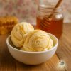 Two big scoops of creamy honeycomb swirl ice cream on a wooden table with a jar of honey in the background
